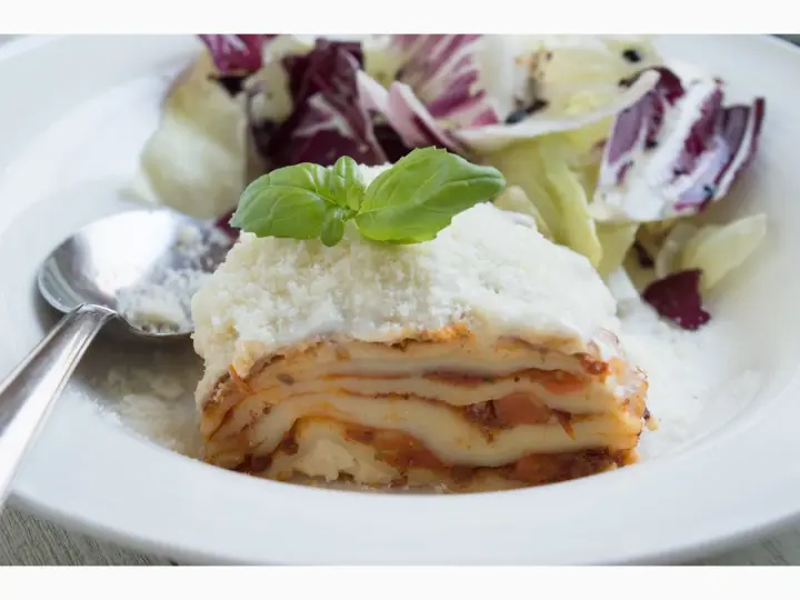 Ein Stück Lasagne mit Schmand, garniert mit Basilikum und Parmesan, serviert mit einem Salat.
