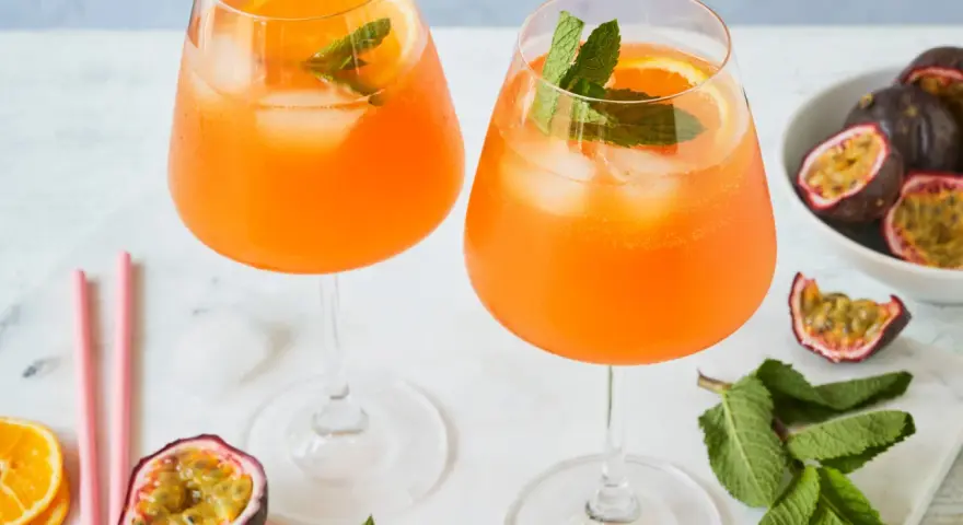 Zwei erfrischende Maracuja Spritz Cocktails mit Eis, Orangenscheiben und Minze, garniert mit frischen Passionsfrüchten.