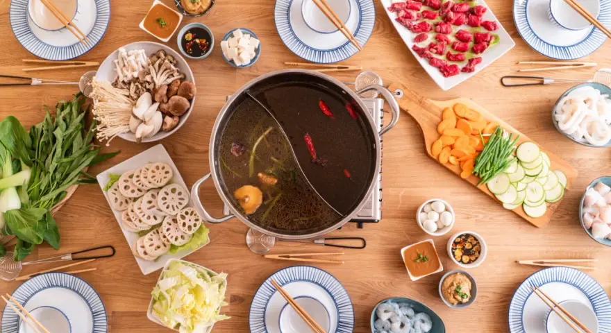 Zutaten für ein köstliches Hot Pot selber machen: Fleisch, Pilze, Gemüse, Garnelen und verschiedene Dips auf einem Holztisch arrangiert.