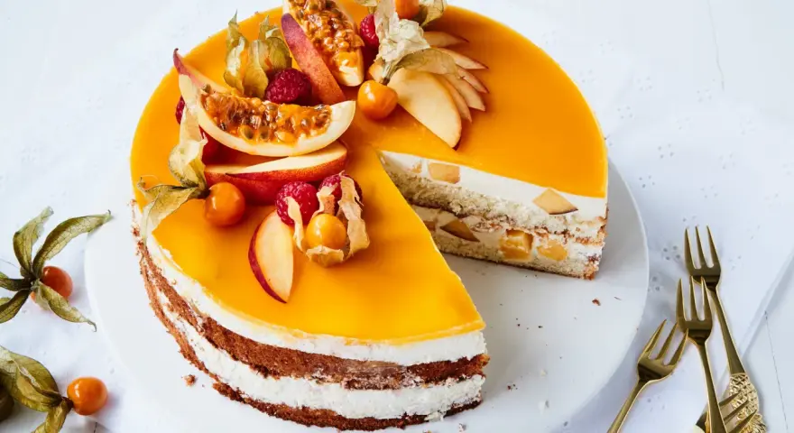 Eine köstliche Pfirsich Maracuja Torte mit frischen Früchten und Sahne. Ein Stück ist bereits angeschnitten.