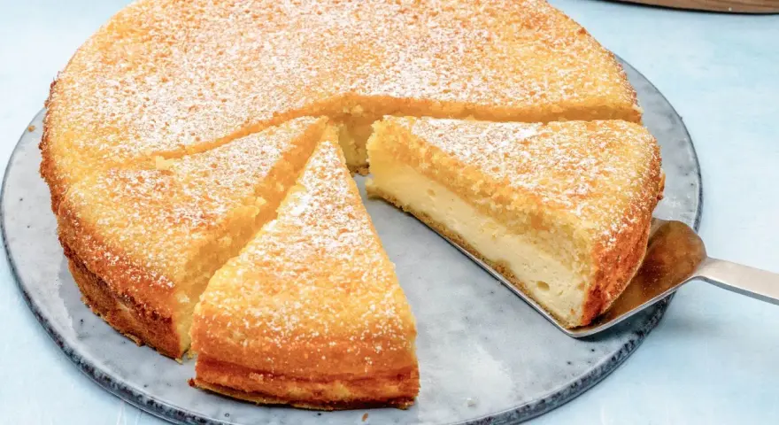 Ein saftiger Käsekuchen, bestäubt mit Puderzucker. Ein Stück wird gerade mit einem Tortenheber herausgehoben. Dreh dich um, Kuchen, du siehst köstlich aus!