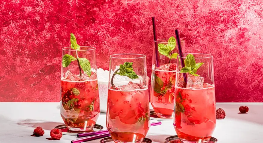 Vier erfrischende Bacardi Razz Mojitos mit Himbeeren und Minze, bereit zum Genießen.