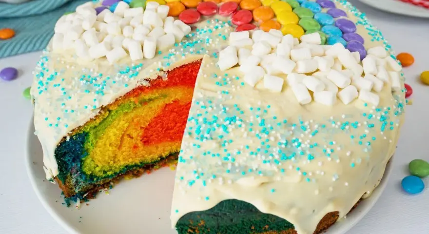 Bunter, sommerlicher Kuchen mit Regenbogen-Schichten, weißen Marshmallows und bunten Smarties.