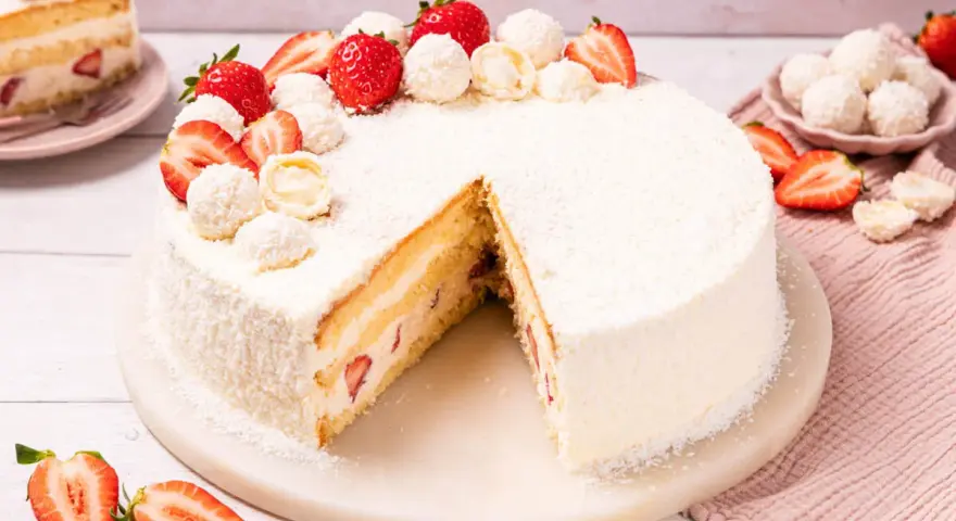Eine köstliche Erdbeer Raffaello Torte, verziert mit frischen Erdbeeren und Raffaello Kugeln, auf einem Marmorsockel.