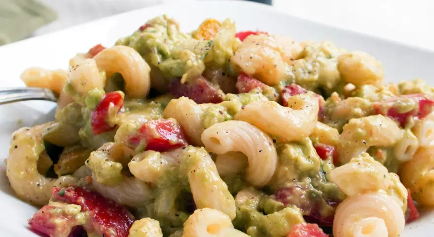 Cremiger nudelsalat mit avocado, Tomaten und Gewürzen auf einem weißen Teller.