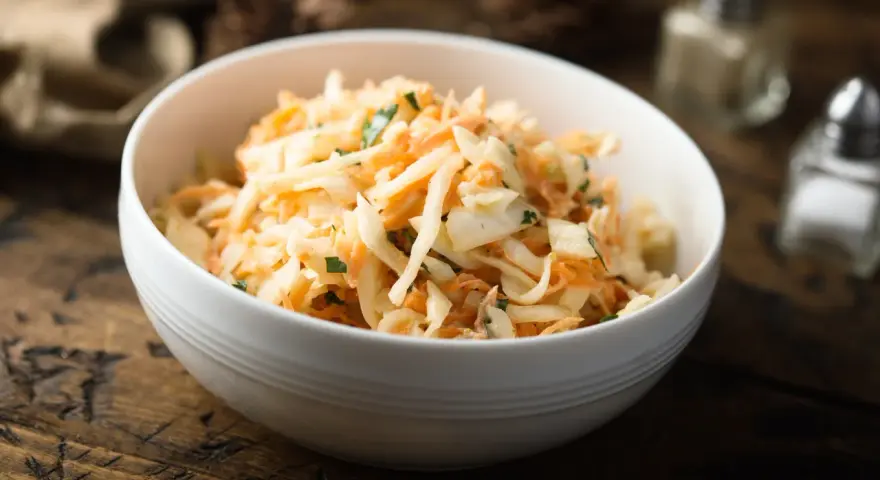 Schüssel mit cremigem Rettichsalat mit Apfel und Kräutern, serviert auf einem rustikalen Holztisch.