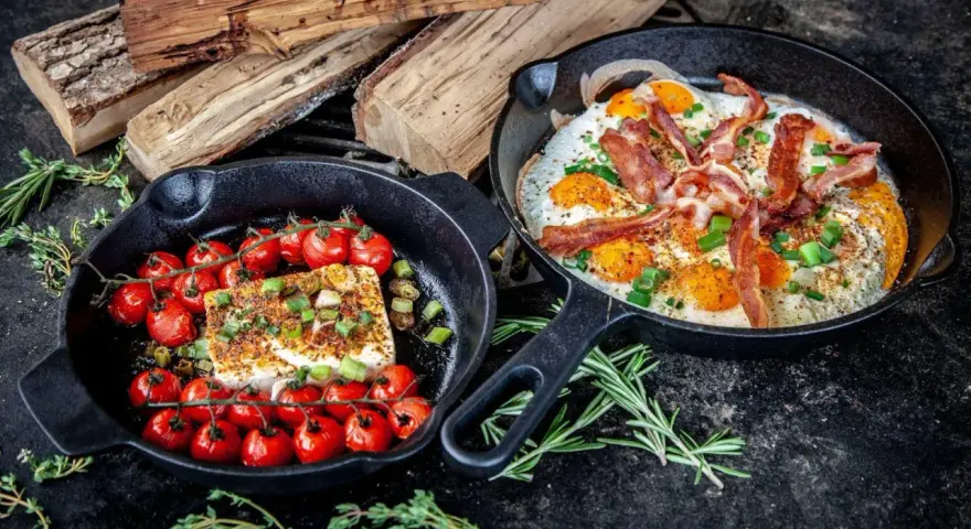 Zwei Gusseisenpfannen mit Eiern, Speck und Kirschtomaten mit Feta – perfekt für low carb grillen.