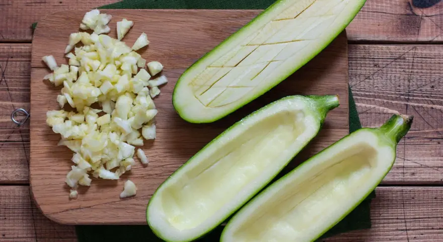 Vorbereitung für gefüllte Zucchini: ausgehöhlte Zucchinihälften und gehackter Knoblauch liegen bereit. Die Zucchini kerne essbar, werden oft mitverwendet.