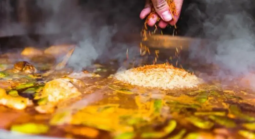 Gewürze werden über Reis und Gemüse gestreut, was zeigt, was ist paella: ein köstliches spanisches Reisgericht, das in einer großen Pfanne gekocht wird.