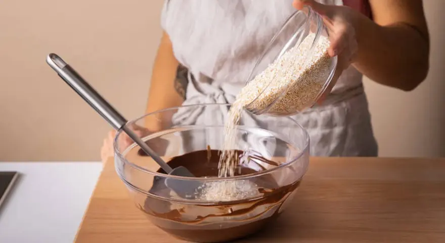 Eine Person gibt Amaranth zu geschmolzener Schokolade in einer Schüssel. Was ist Amaranth? Ein gesundes Getreide für leckere Rezepte.