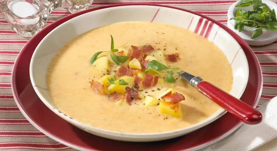 Eine dampfende, cremige Kartoffelsuppe mit Sahne, garniert mit Kartoffelwürfeln, knusprigem Speck und frischen Kräutern.