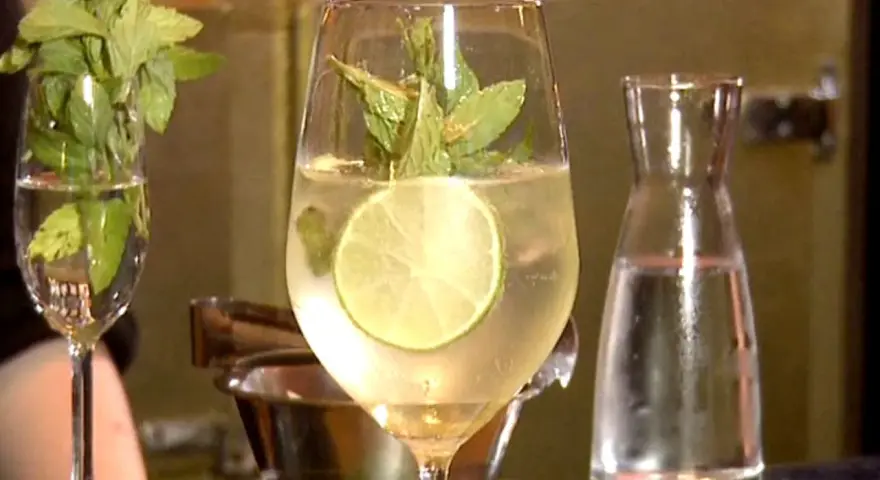 Erfrischender Hugo mit Limette und Minze, perfekt für ein Hugo Rezept. Daneben ein Glas mit Minze und eine Karaffe Wasser.