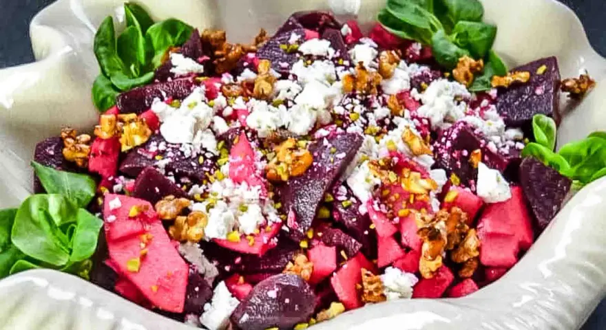 Rote Bete Salat mit Apfel, Feta und Walnüssen, garniert mit grünen Blättern. Ein farbenfroher und gesunder Genuss.