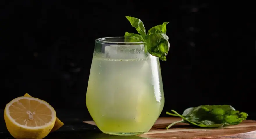 Erfrischender Basil Smash mit Zitrone und Basilikum garniert, serviert auf einem Holzbrett.