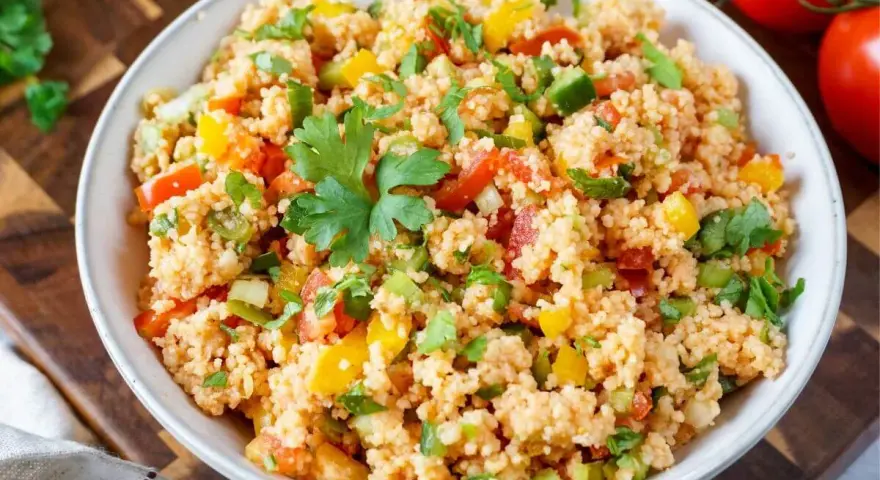 Frischer Couscous Salat mit Tomaten, Paprika und Petersilie, garniert mit einem Petersilienblatt.