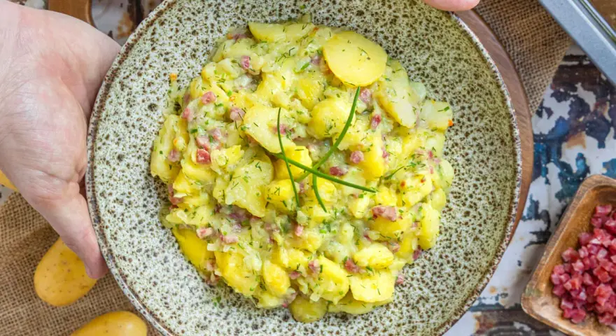 Ein Teller mit herzhaftem Kartoffelsalat mit Speck und frischen Kräutern, bereit zum Servieren.