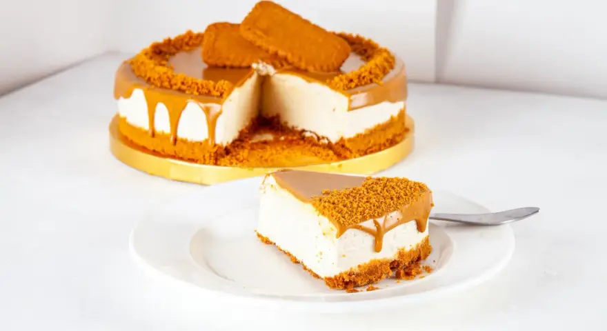 Ein Stück cremiger Lotus Cheesecake ohne Backen, mit Karamellglasiert und Keksbröseln bestreut.