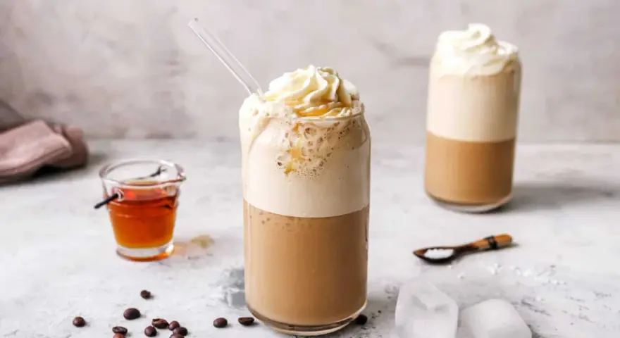 Eiskaffee selbst machen: Ein erfrischender Eiskaffee mit Sahne und Sirup, daneben Kaffeebohnen und Eiswürfel.