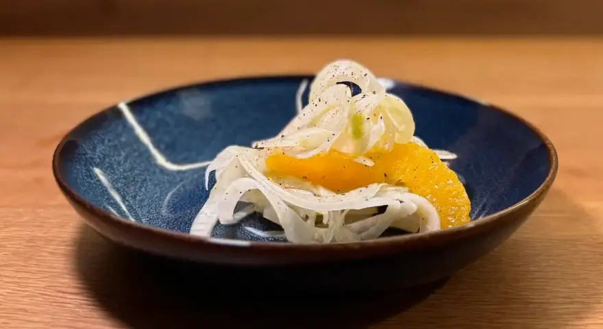 Ein erfrischender Fenchel-Orangen-Salat, garniert mit Pfeffer, in einer blauen Schale auf einem Holztisch.