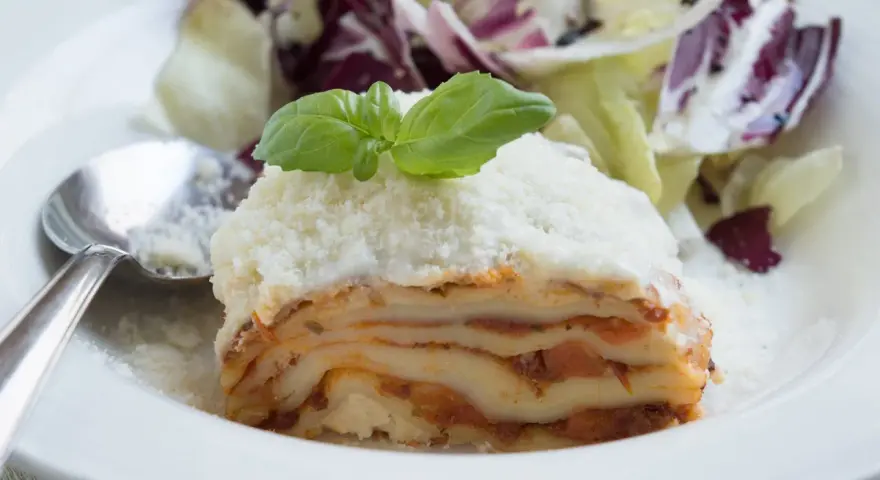 Ein Stück Lasagne mit Schmand, garniert mit Basilikum und Parmesan, serviert mit einem Salat.