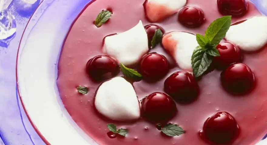 Erfrischende Kirschsuppe mit Sago, garniert mit Kirschen, Minze und weißen Tupfern.