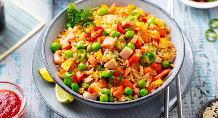 Schüssel mit Nasi Goreng: gebratener Reis mit Hühnchen, Erbsen, Karotten, Chili und Limettenspalten.