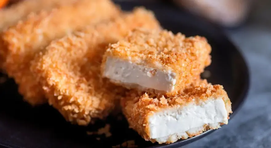 Knusprig gebratenes Tofu auf einem Teller. Die goldbraune Panade umhüllt das weiche Innere. Perfekt, um Tofu knusprig braten zu lernen.