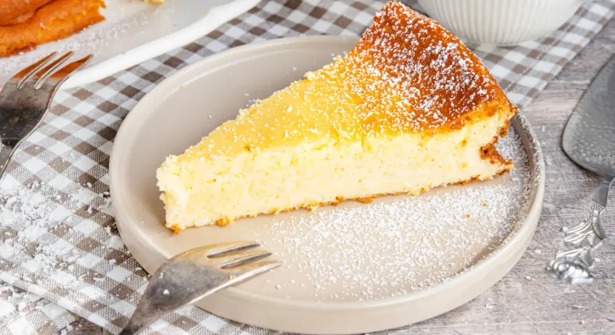 Ein saftiges Stück Kokoskuchen mit Pudding, gebacken in einer Springform, bestäubt mit Puderzucker.
