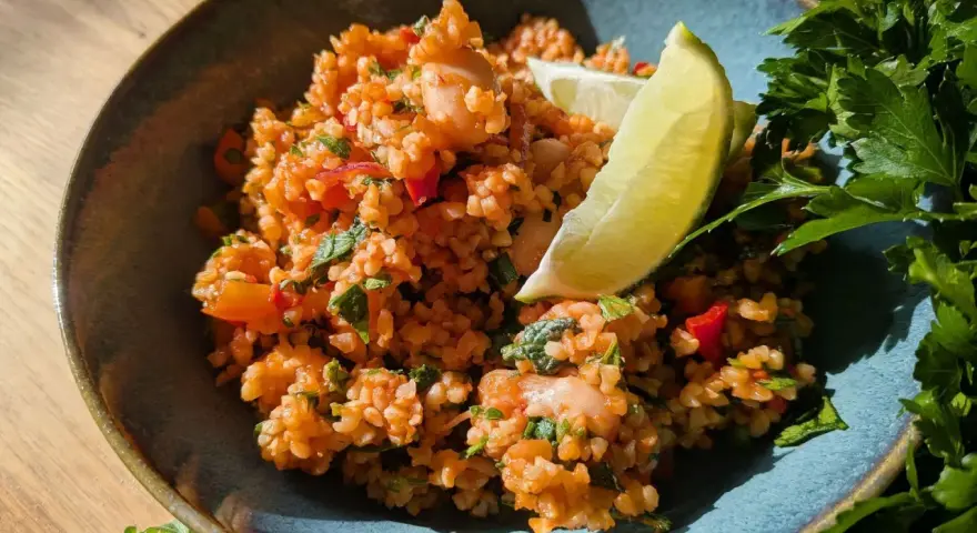 Ein erfrischender bulgursalat mit minze, garniert mit Limettenspalten und frischer Petersilie.