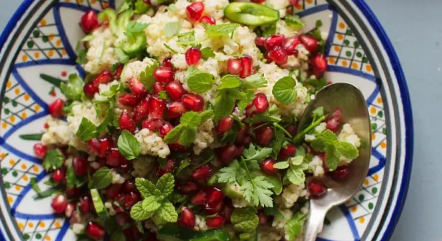 Bunter Couscous-Salat mit Granatapfelkernen, Minze und Petersilie in einer orientalisch gemusterten Schale.