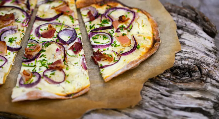 Flammkuchen mit klassischem Belag: Speck, Zwiebeln und Schnittlauch auf knusprigem Teig.