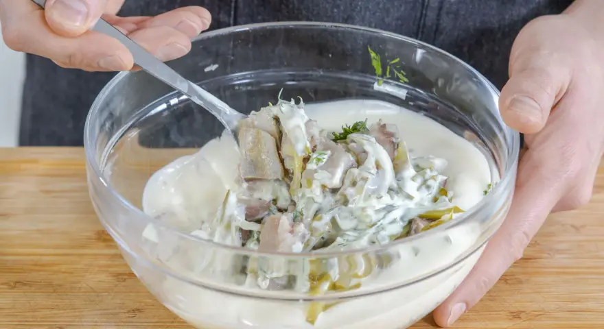 Matjes Hausfrauenart, Omas Rezept: Ein Löffel voll cremiger Sauce mit Matjesstücken und Dill wird aus einer Glasschüssel gehoben.