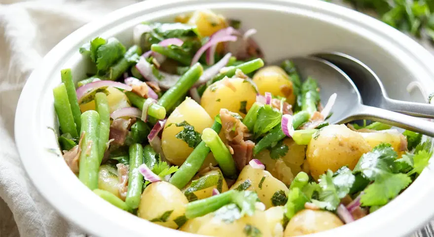 Frischer Kartoffel Bohnen Salat mit roten Zwiebeln und Kräutern in einer weißen Schüssel, bereit zum Servieren.