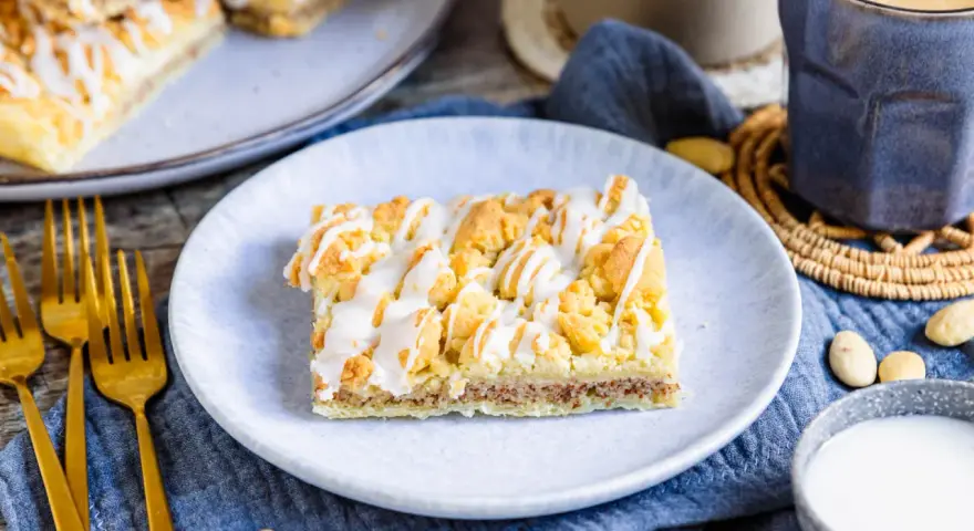 Ein Stück Prasselkuchen, wie aus einem DDR-Rezept, mit Zuckerguss und Streuseln. Dazu Kaffee und Mandeln.