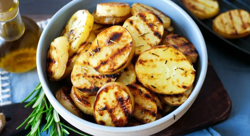 Schmackhafte Kartoffelscheiben mit Rosmarin, perfekt gegrillt. Die Streifen vom Grill sind deutlich sichtbar.