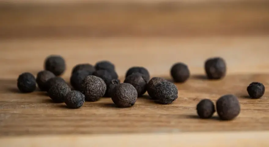 Eine Gruppe von Pimentkörnern liegt auf einem Holzbrett. Was ist Piment? Diese aromatischen Beeren duften nach Zimt, Nelken und Muskat.