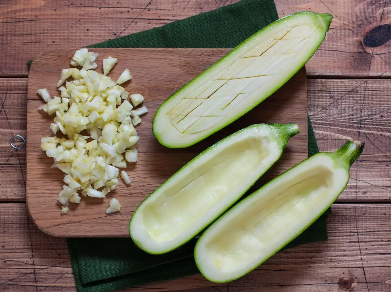Vorbereitung f&uuml;r gef&uuml;llte Zucchini: ausgeh&ouml;hlte Zucchinih&auml;lften und gehackter Knoblauch liegen bereit. Die Zucchini kerne essbar, werden oft mitverwendet.