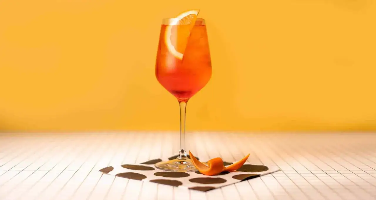 Ein Aperol Spritz Rezept Original: Ein Glas mit leuchtend orangem Aperol Spritz, garniert mit einer Orangenscheibe und einem Spiral-Twist aus Orangenschale.