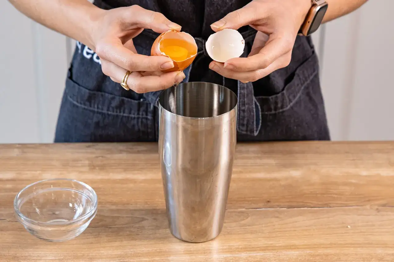 H&auml;nde geben ein Ei in einen Cocktail-Shaker. Ein cremiger Cocktail mit Ei wird zubereitet.