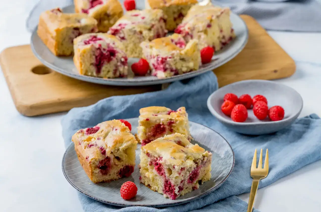 Saftiger Kuchen mit Himbeeren, auf einem Teller angerichtet, daneben eine kleine Schale mit frischen Himbeeren.