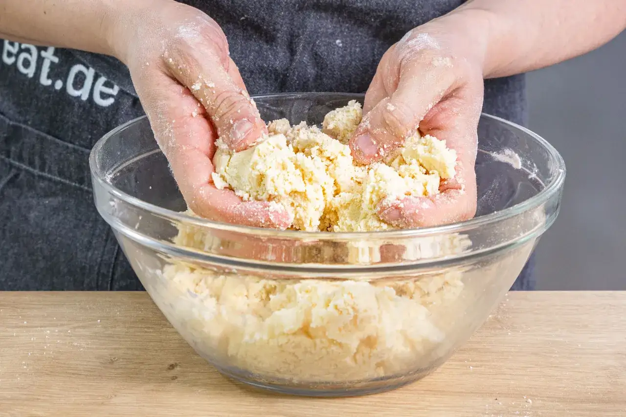 Hände verarbeiten Teig für ein einfaches Streusel Rezept in einer Glasschüssel.