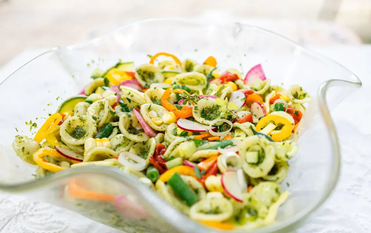Bunter Nudelsalat ohne Mayonnaise mit Orecchiette, Paprika, Radieschen und Kräutern in einer Glasschüssel.