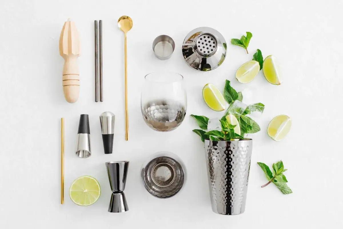 Alles für Ihre besten Cocktail Rezepte: Shaker, Glas, Limetten, Minze und Zubehör auf weißem Hintergrund.