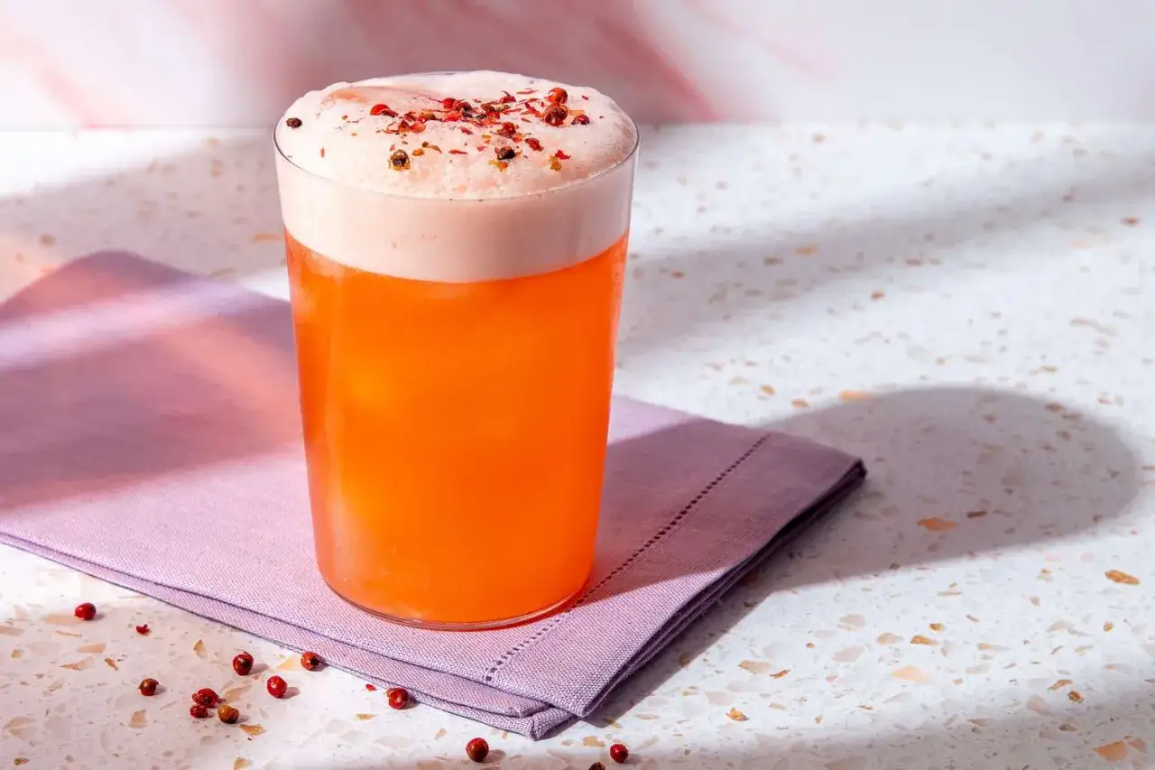 Ein erfrischender Aperol Sour mit cremigem Schaum und rosa Pfefferbeeren.