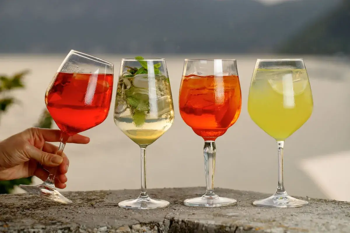 Vier Gl&auml;ser mit Aperol Spritz Varianten, darunter ein roter, ein heller mit Minze, ein klassischer Aperol und ein gelber Drink.