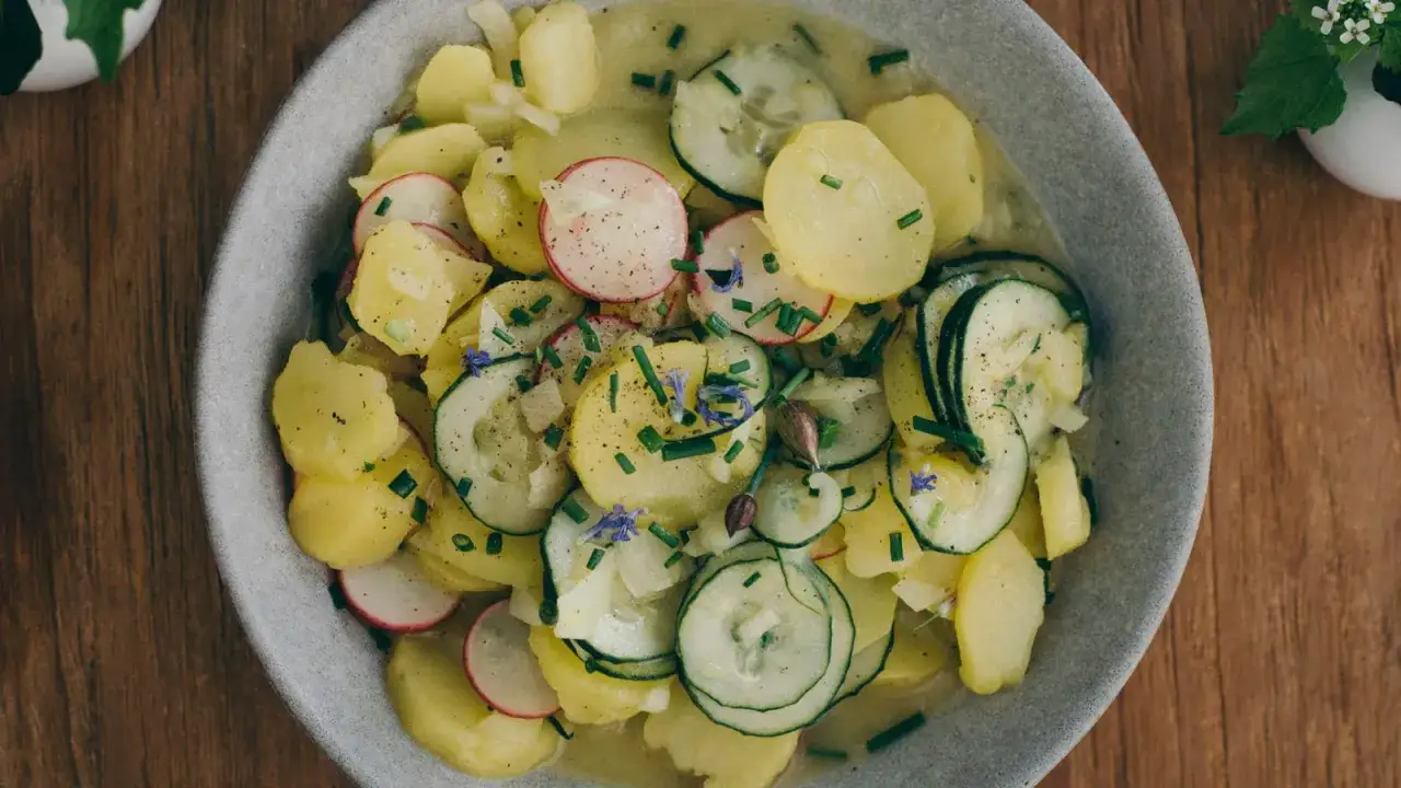 Ein Teller mit lauwarmer bayrischer Kartoffelsalat, garniert mit Radieschen, Gurken und Schnittlauch.