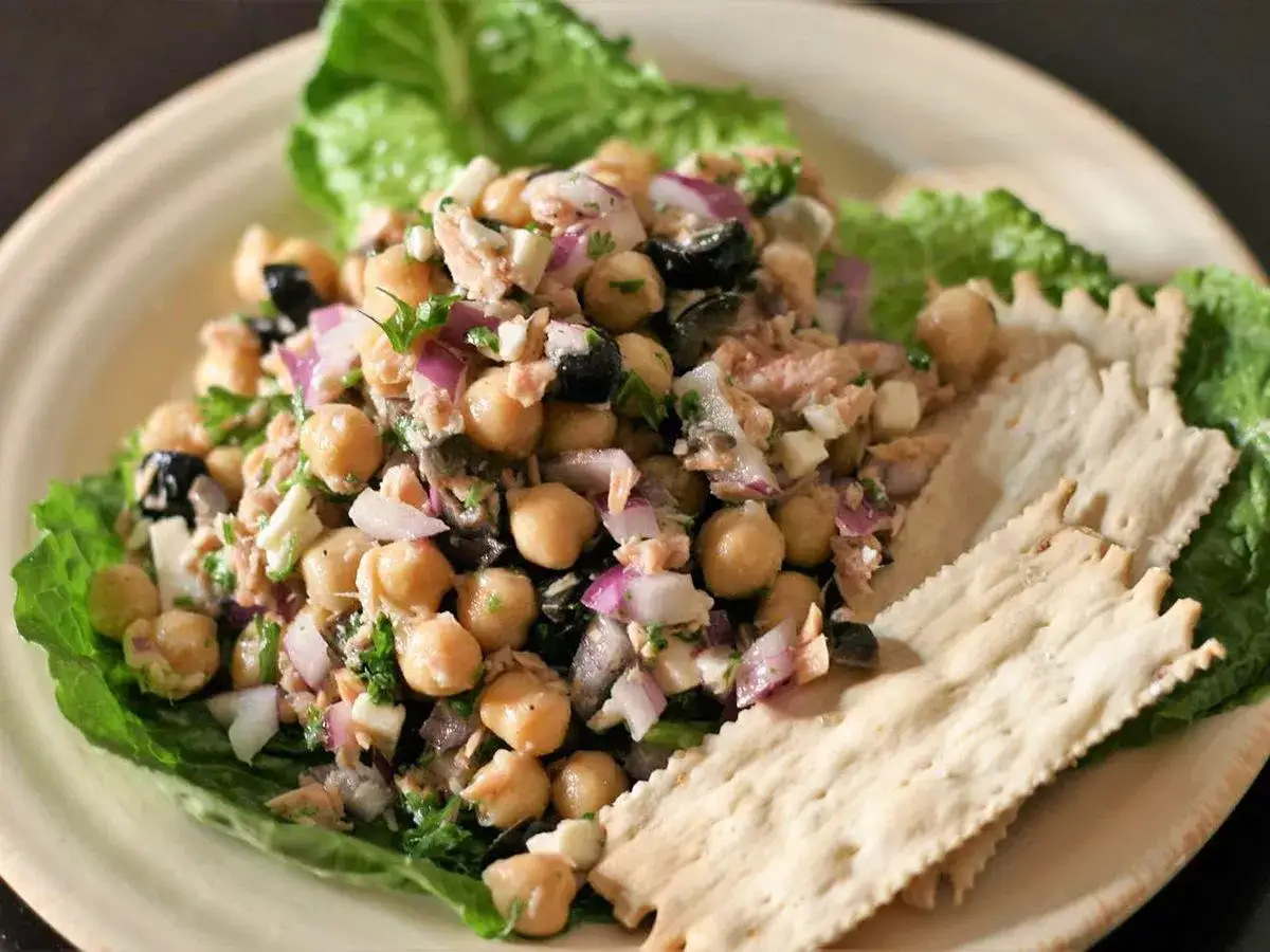 Kichererbsen Thunfisch Salat mit Oliven, Zwiebeln und Petersilie auf Salatblatt, serviert mit Crackern.