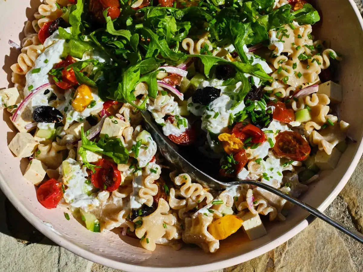 Ein bunter Kritharaki Salat mit cremiger So&szlig;e, Kirschtomaten, Gurken, Oliven und Rucola.