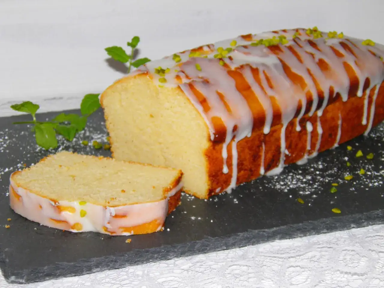 Saftiger Kuchen mit vielen Eiern, überzogen mit Zuckerguss und bestreut mit Pistazien. Ein Stück ist bereits angeschnitten.