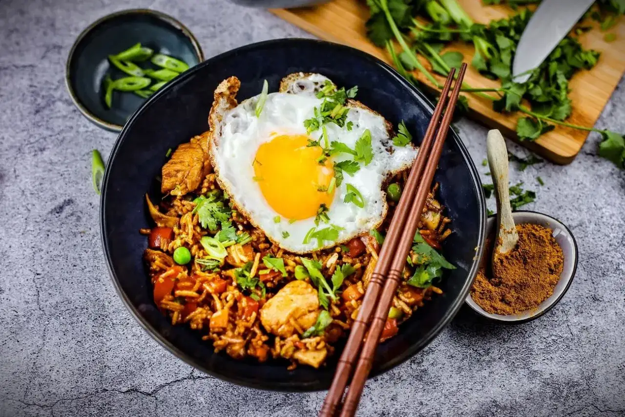 Nasi Goreng: Gebratener Reis mit H&uuml;hnchen, Erbsen, Karotten und einem Spiegelei, garniert mit Koriander und Fr&uuml;hlingszwiebeln.